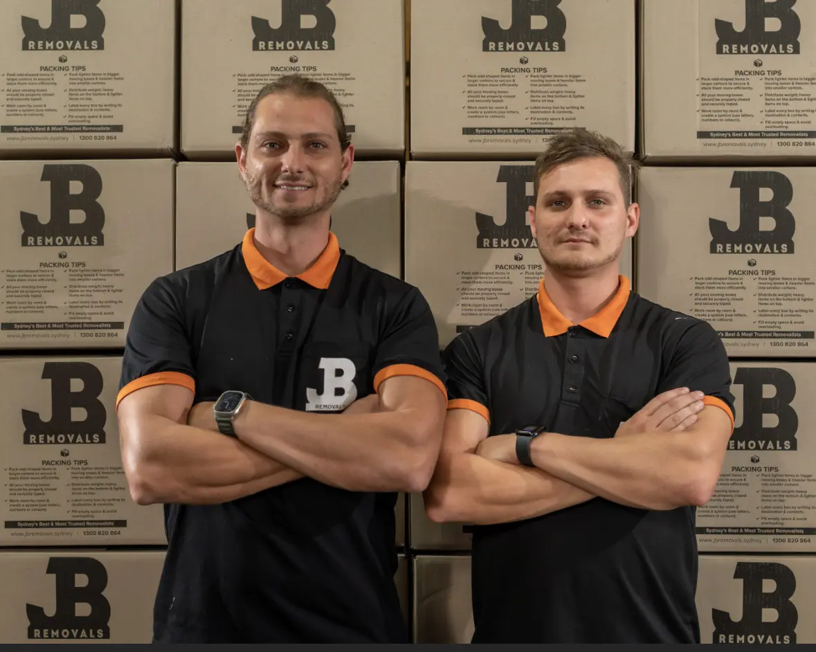Two uniformed JB team members beside stacked cartons