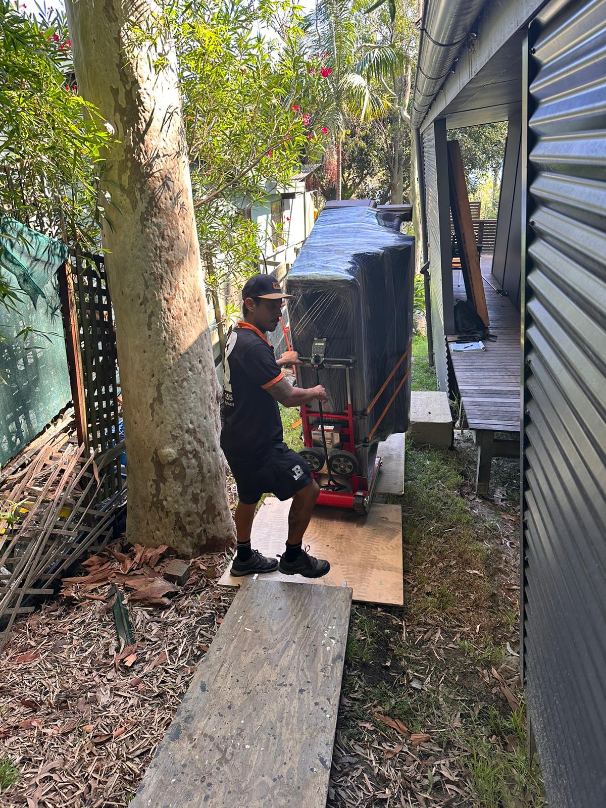 JB Removals moving a wrapped upright piano through narrow side access
