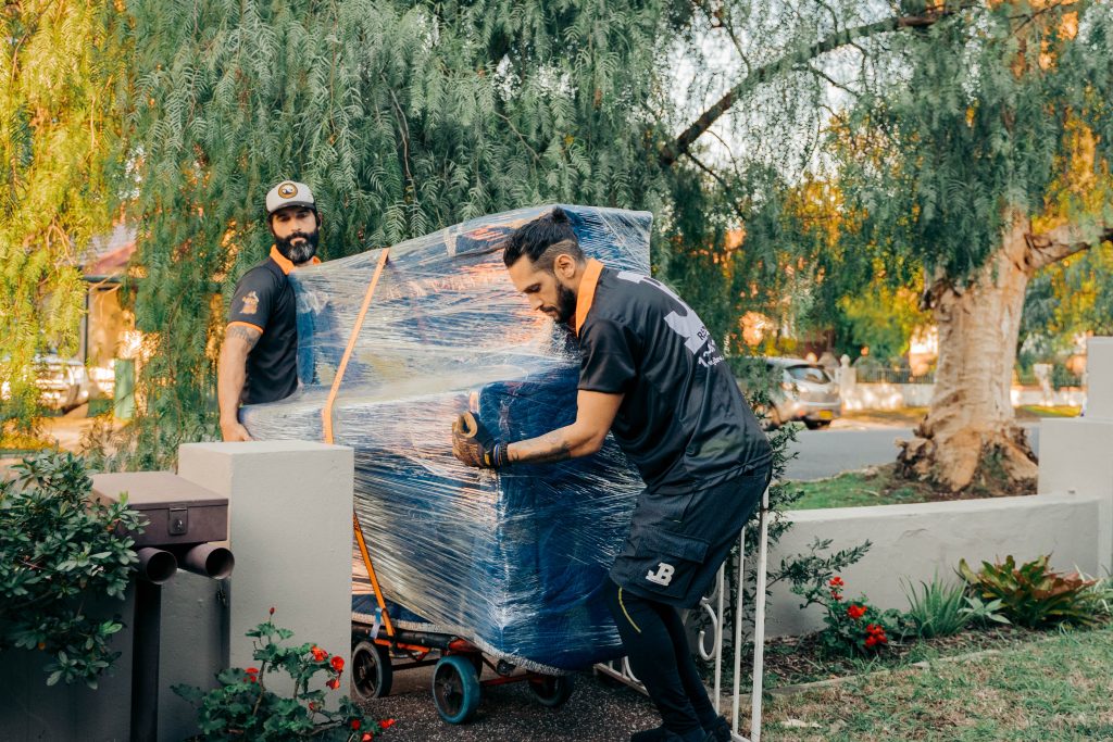 Two JB movers guiding a wrapped item on a trolley along a garden path