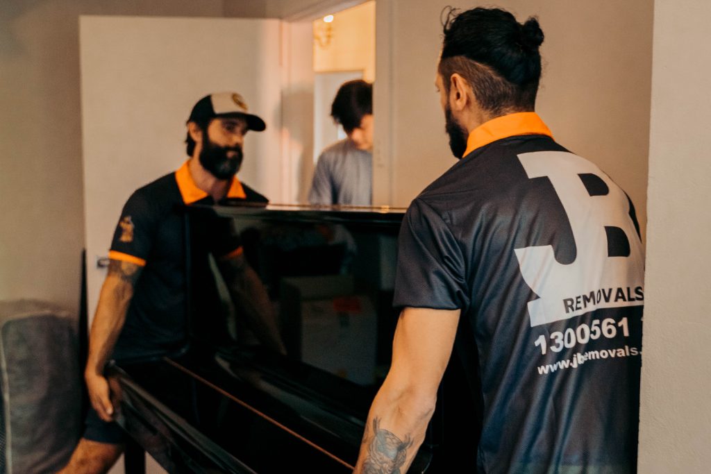 JB crew moving an upright piano through an interior doorway