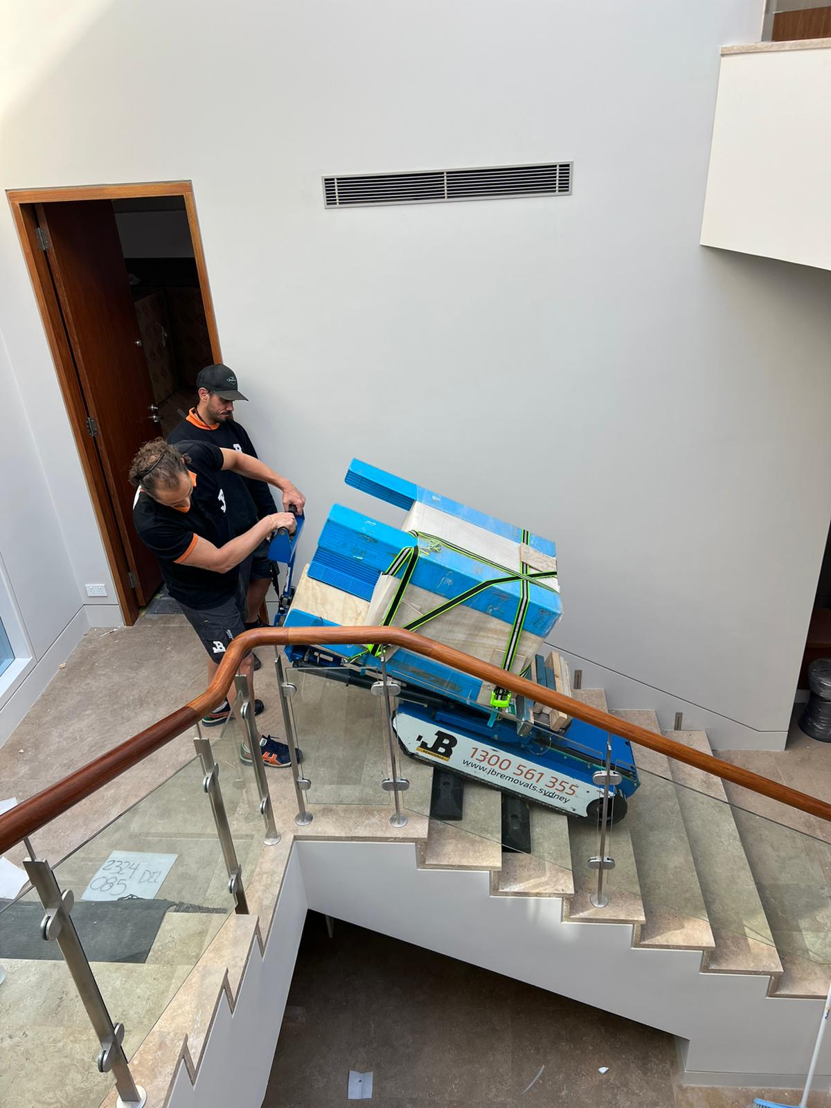 Two JB Removals crew members guiding a strapped item on stair-climbing equipment