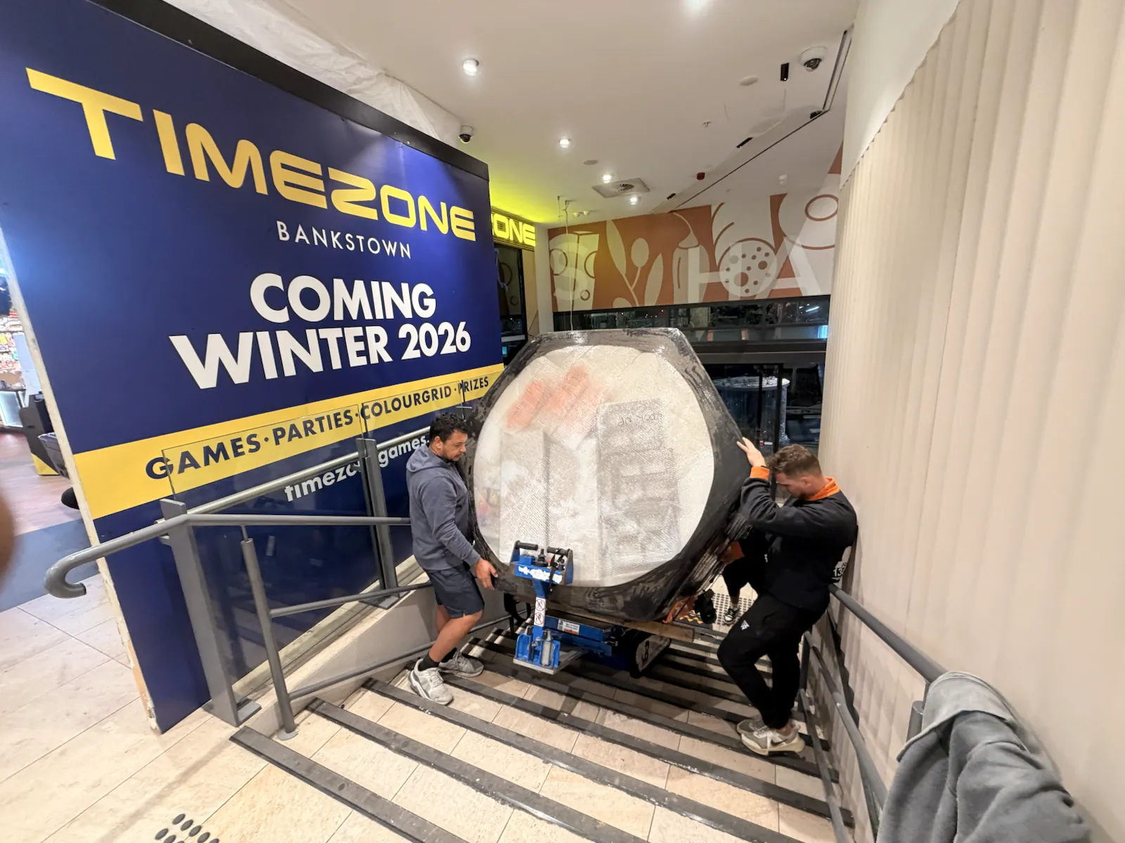 JB Removals crew guiding a protected glass arcade machine down a commercial staircase