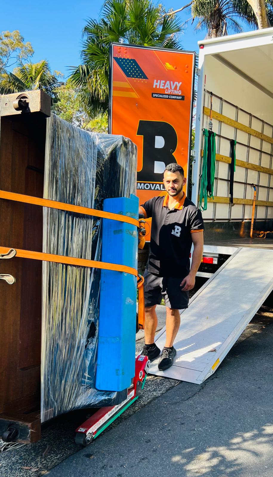 Wrapped upright piano beside a JB heavy-lifting truck ramp