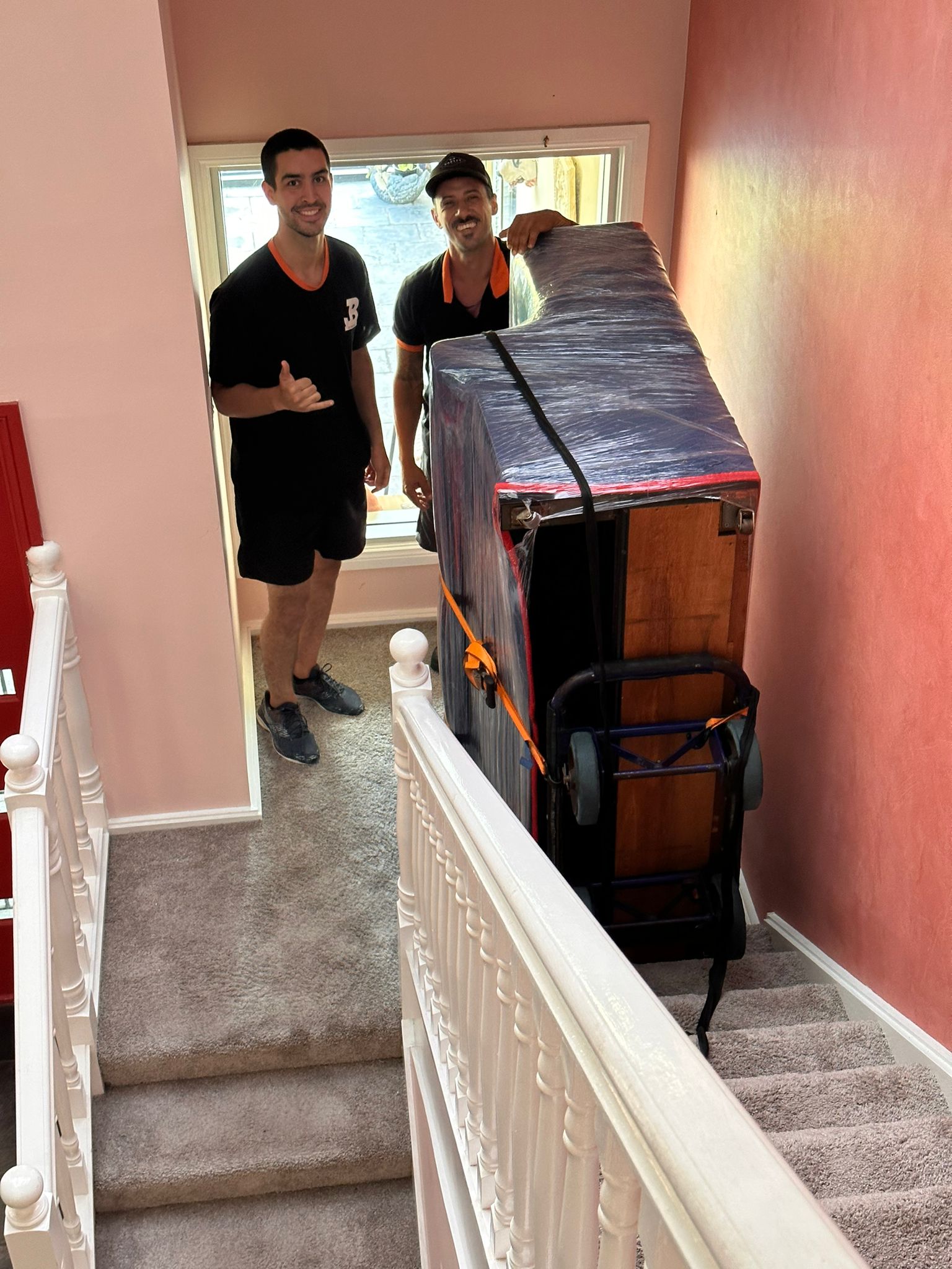 JB Removals crew positioning a wrapped upright piano on residential stairs