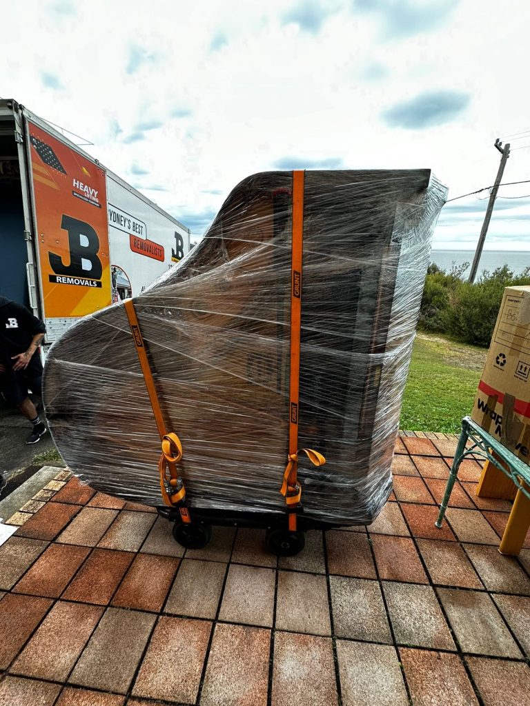 Wrapped upright piano beside a JB Removals truck during a specialist move
