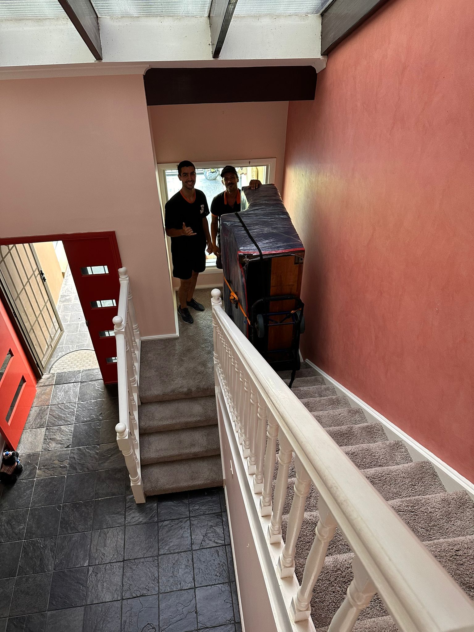 JB Removals crew moving a wrapped upright piano on a staircase