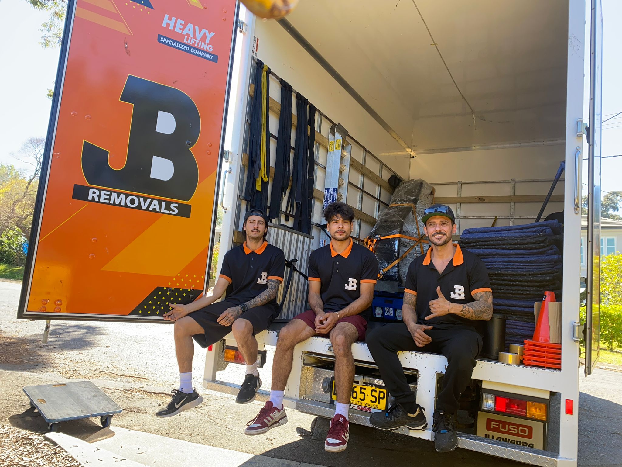 Three JB crew members seated at the rear of a branded moving truck