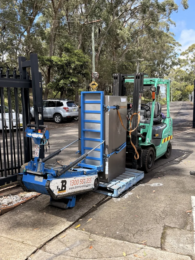 Blue stair-climbing equipment beside a forklift and vehicle outside the site