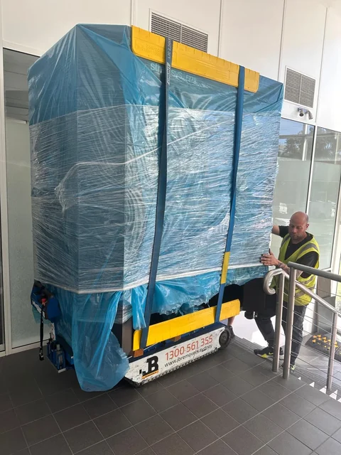 Large wrapped item restrained on a blue stair climber beside a tiled landing and metal handrail