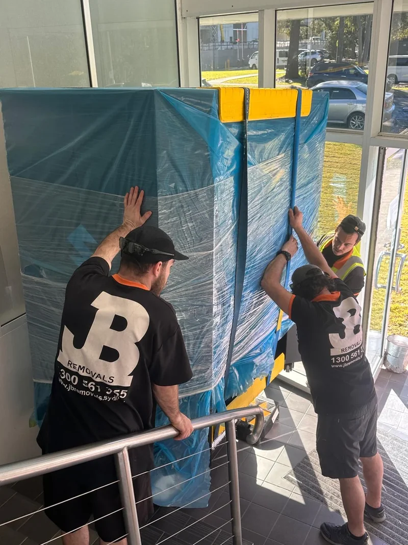 JB Removals crew attending the wrapped industrial item in a restricted stairway beside a metal balustrade