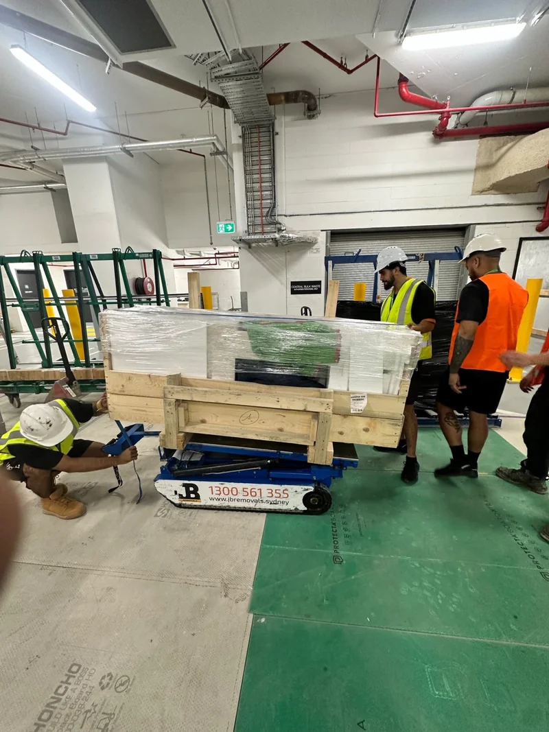 JB crew beside timber-framed equipment on a tracked handling platform over floor protection.