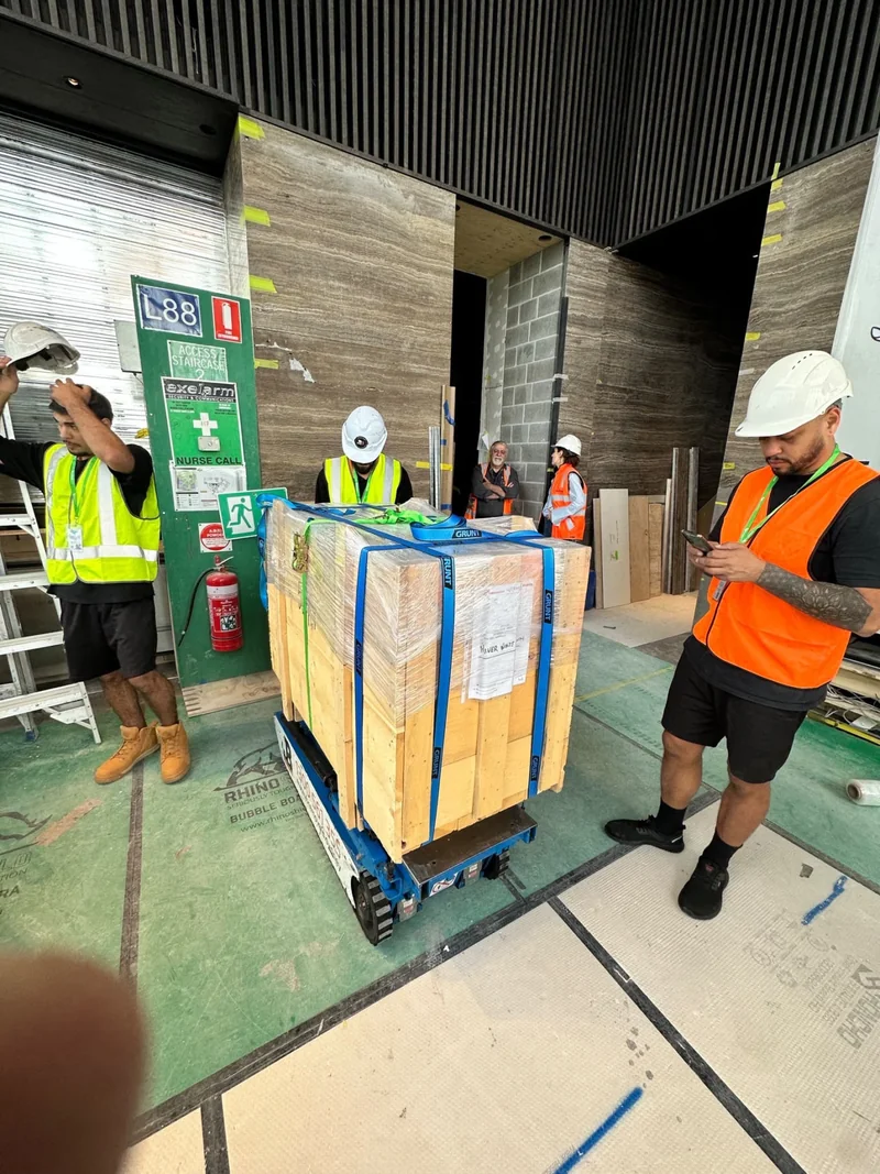JB Removals crew in hard hats and high-visibility clothing beside a wrapped crate on a tracked platform.