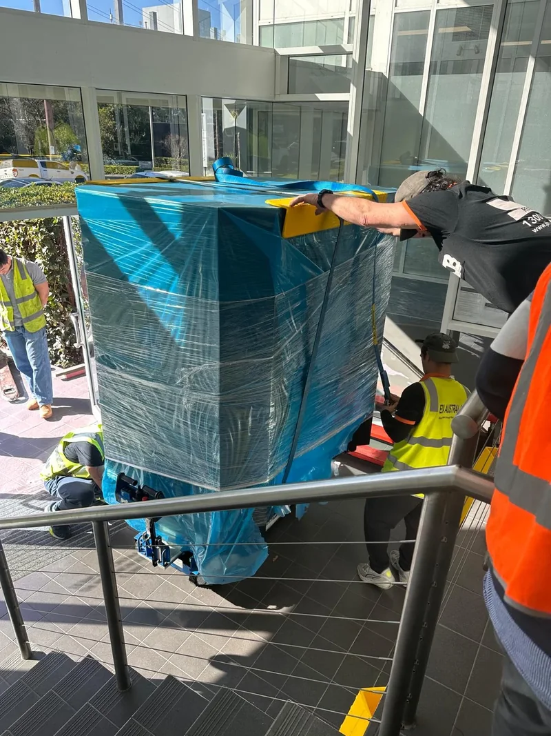 Protected industrial equipment on powered moving equipment along a tiled stair route with crew nearby