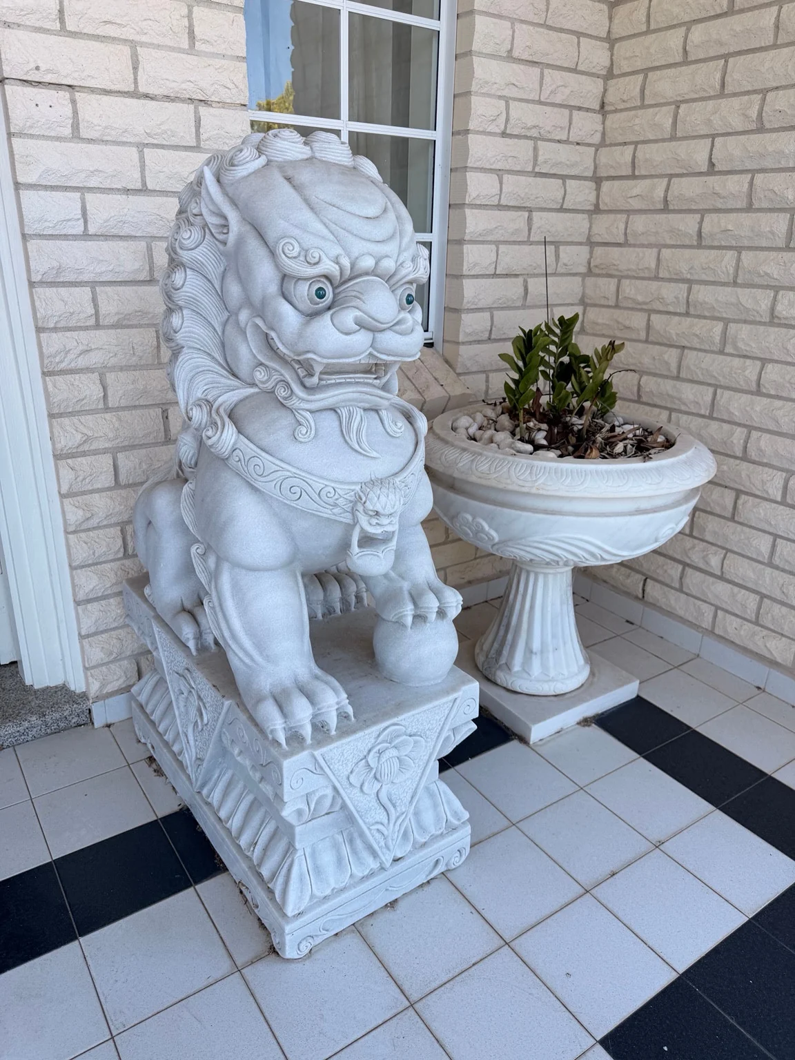Carved guardian lion with a paw resting on a ball beside a pedestal planter