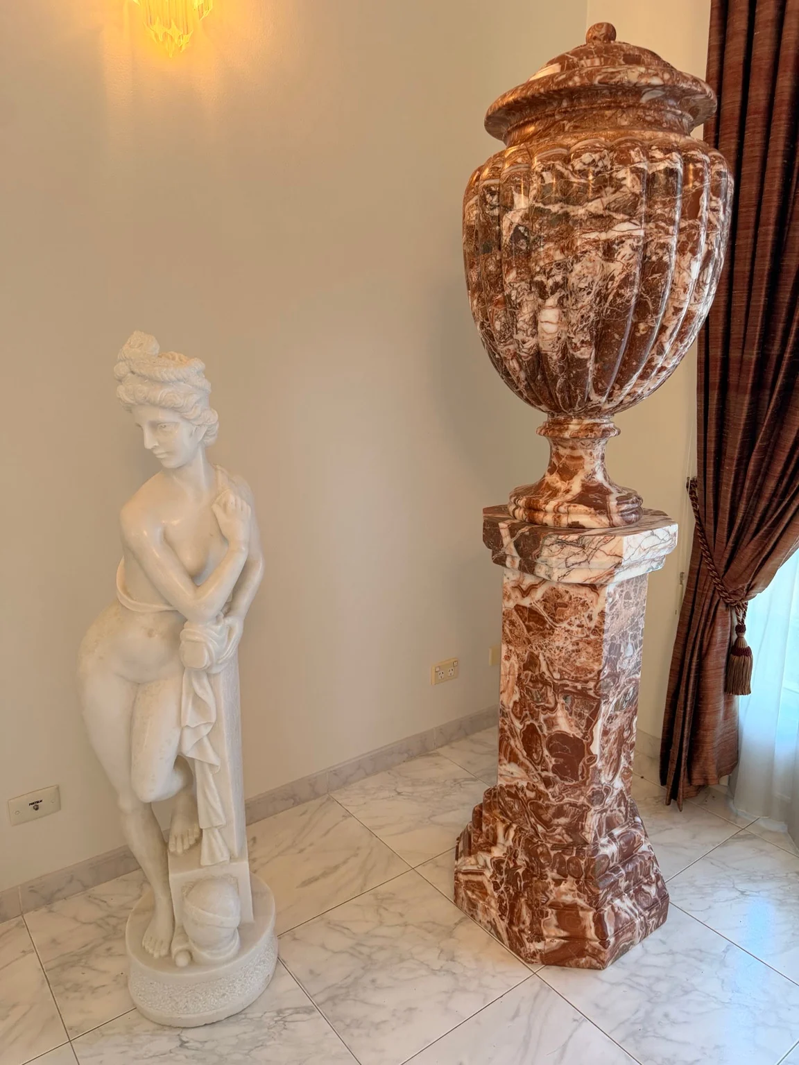 White figurative statue beside a red-and-white veined decorative urn on a tall pedestal