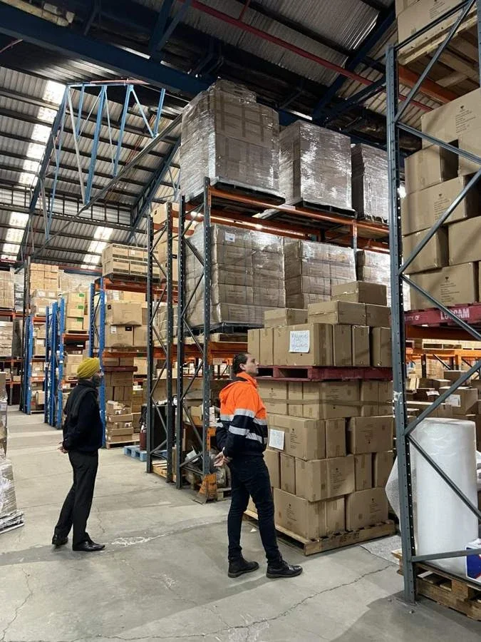 Two people reviewing palletised stock and warehouse racking, with one wearing high-visibility workwear