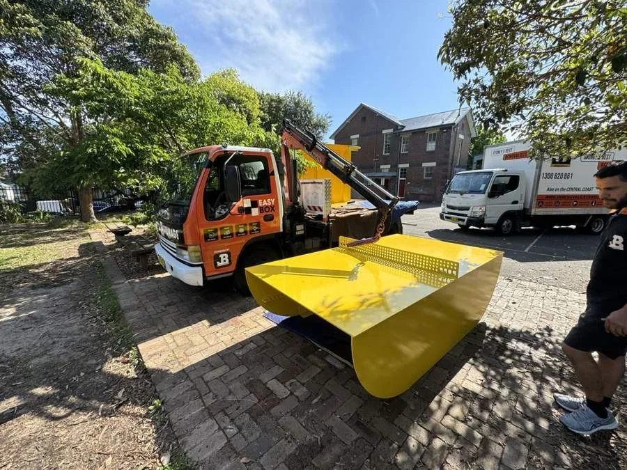 Yellow metal outdoor table-tennis table beside a JB crane truck during delivery