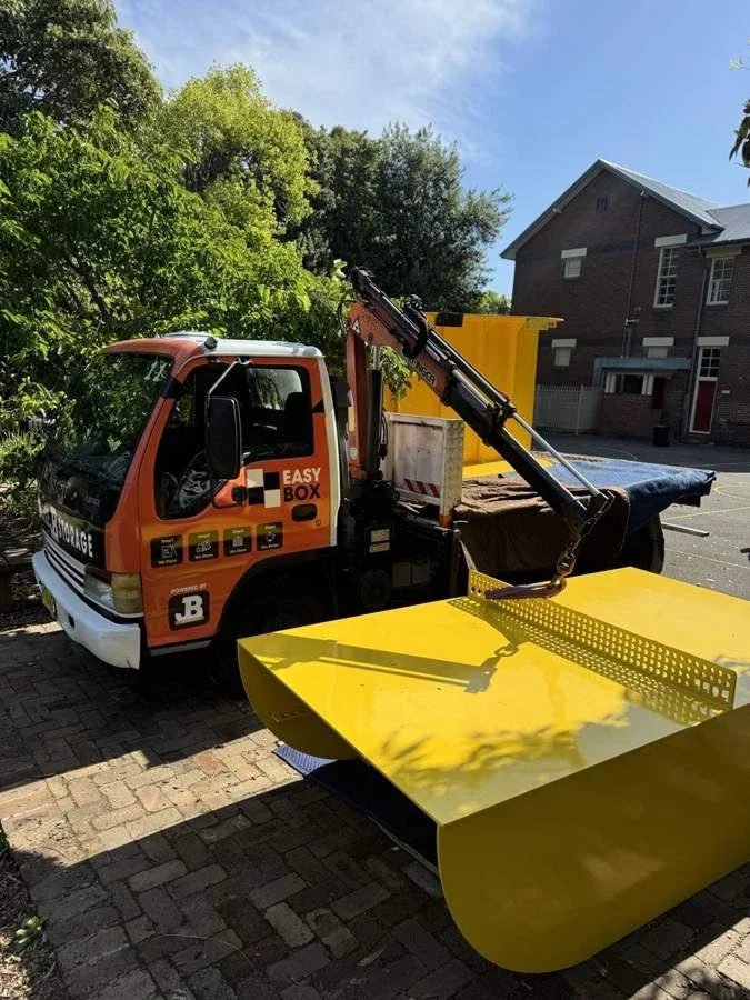 Truck-mounted crane beside the yellow metal table-tennis table and its perforated net