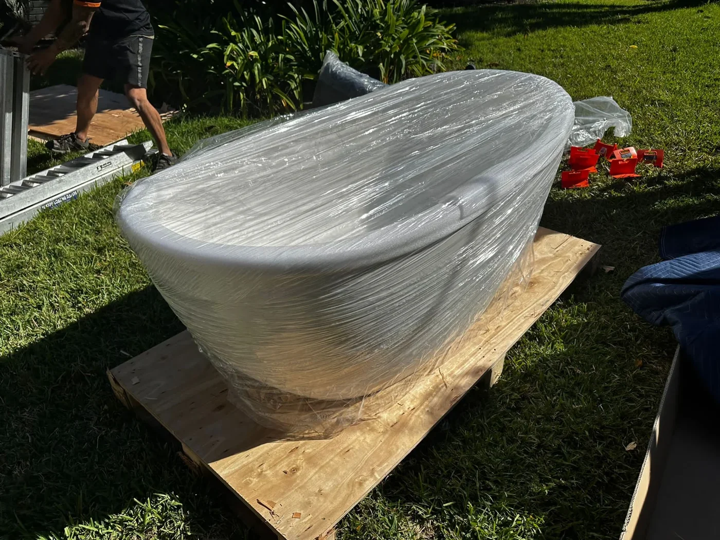 White freestanding bath wrapped in clear film on a timber board outdoors