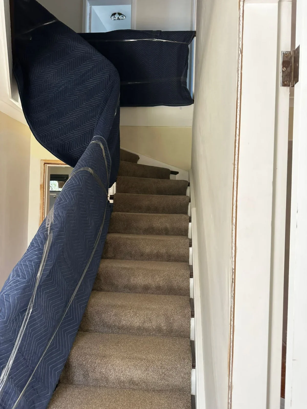 Carpeted staircase with a turn and protective blankets over adjoining surfaces