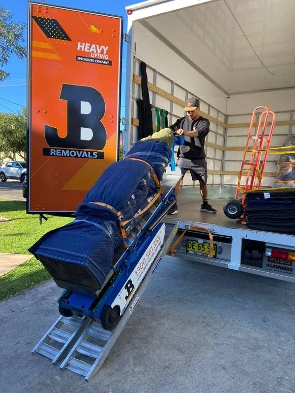 JB operator with a wrapped statue secured to powered moving equipment on a metal ramp at the removalist truck