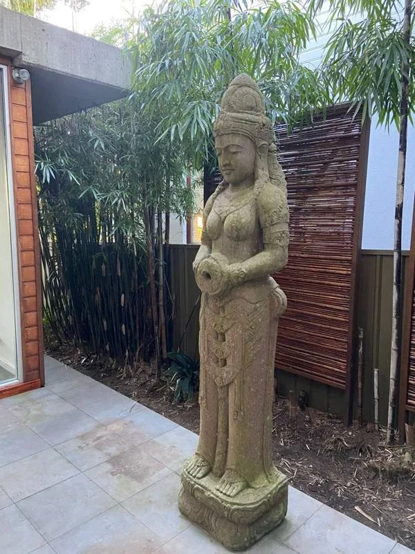 Tall carved garden figure on a decorative base beside bamboo and courtyard paving