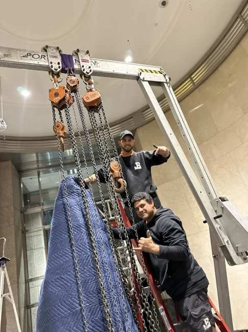 Team members beside the gantry with chain hoists and padded stone visible