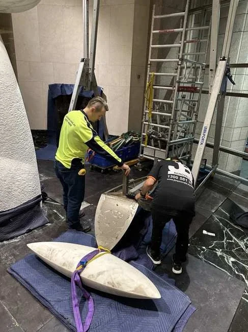 Two team members beside separated marble pieces with straps and floor blankets
