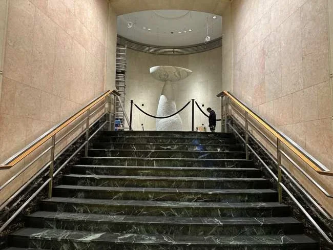 Marble stairs and railings leading towards the sculpture in the building lobby