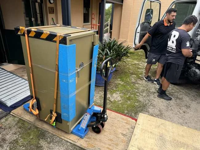 Padded safe strapped within a blue handling frame near a JB truck