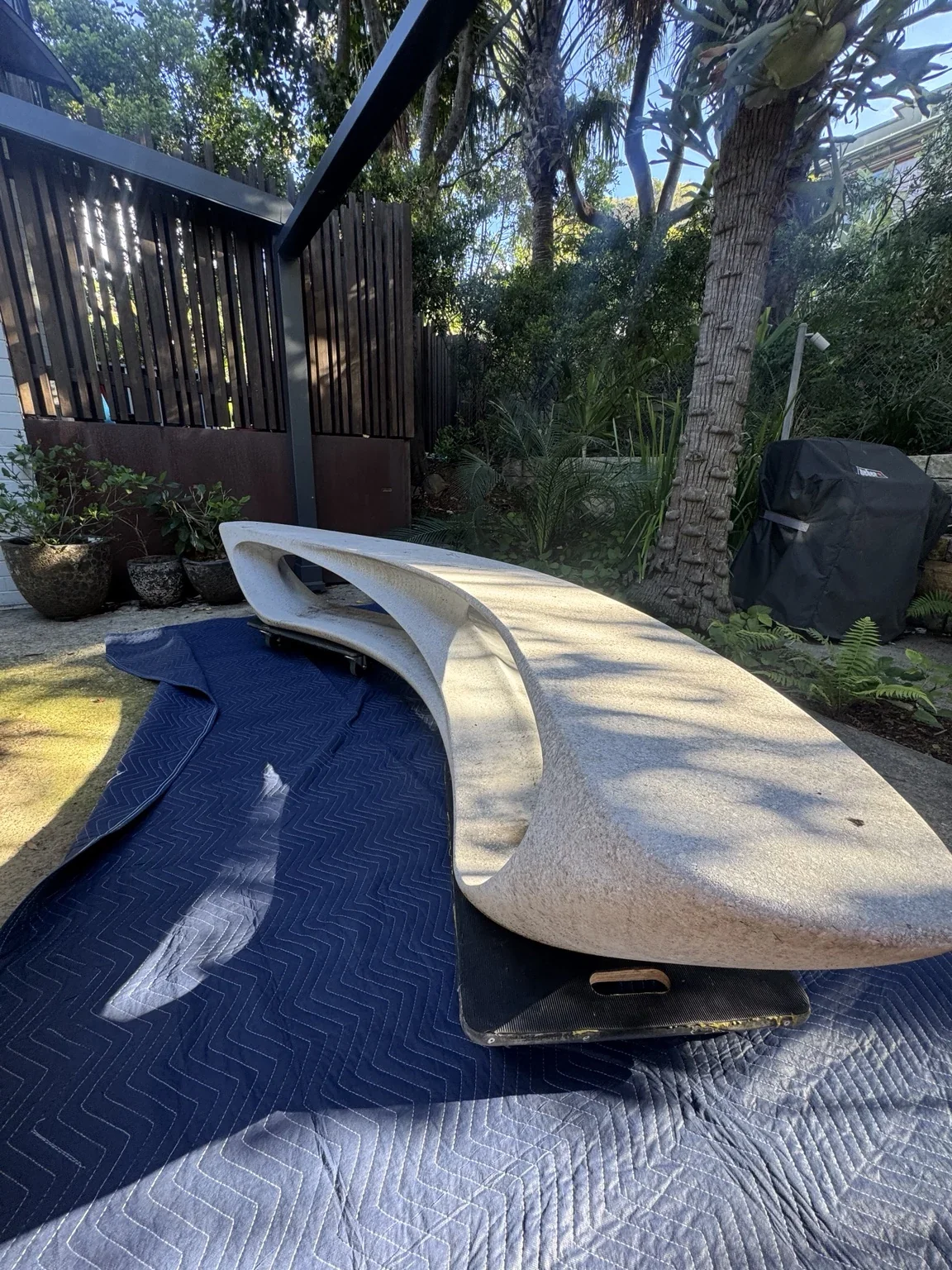 Unwrapped curved marble bench resting above protective blankets outdoors