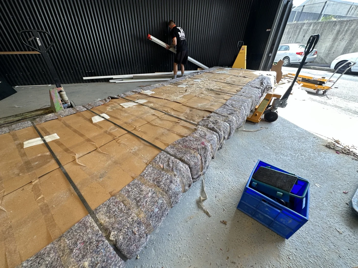 Wrapped oversized tabletop with protective blankets, cardboard and pallet jacks nearby