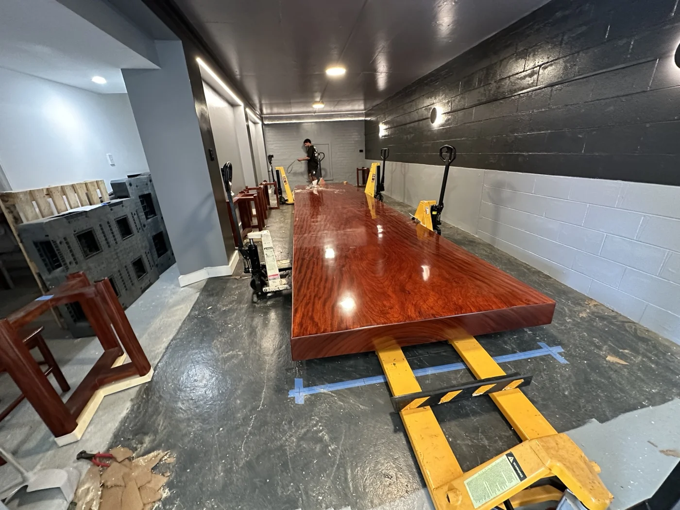 Long polished timber tabletop supported by lifting equipment with stands positioned beside it