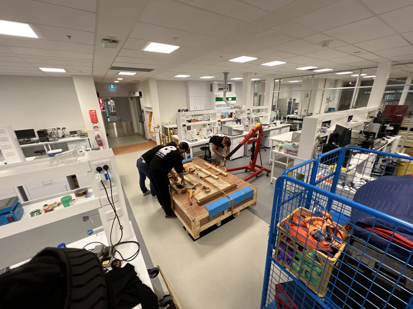 JB crew working around the crated optical table and red hydraulic workshop crane inside a laboratory