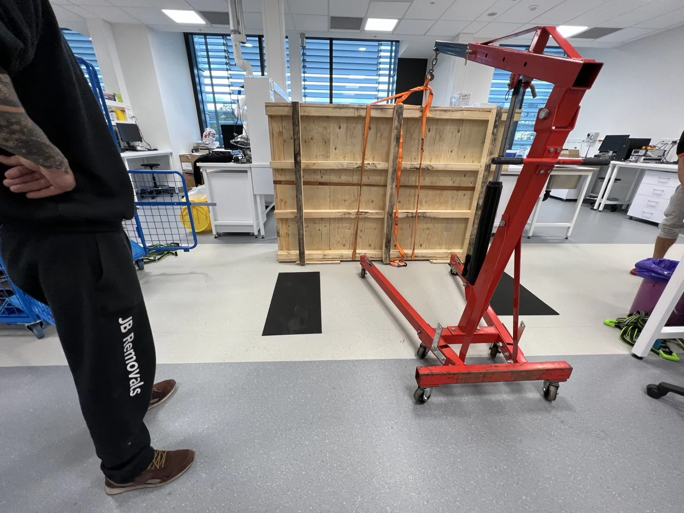 Portable red hydraulic workshop crane beside upright timber crate panels in the laboratory