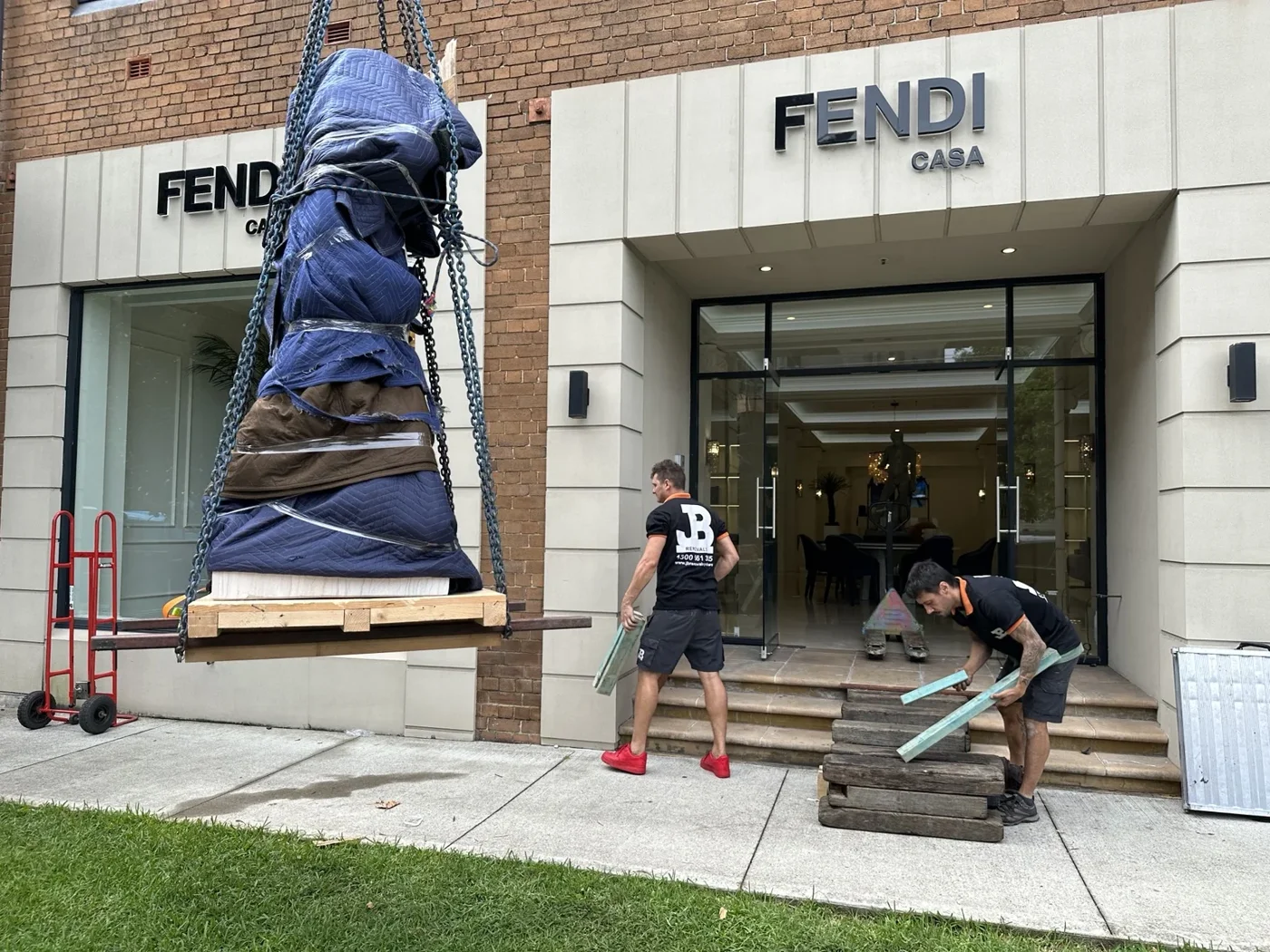 Blanket-wrapped statue supported on a timber pallet during a crane lift at Fendi Casa