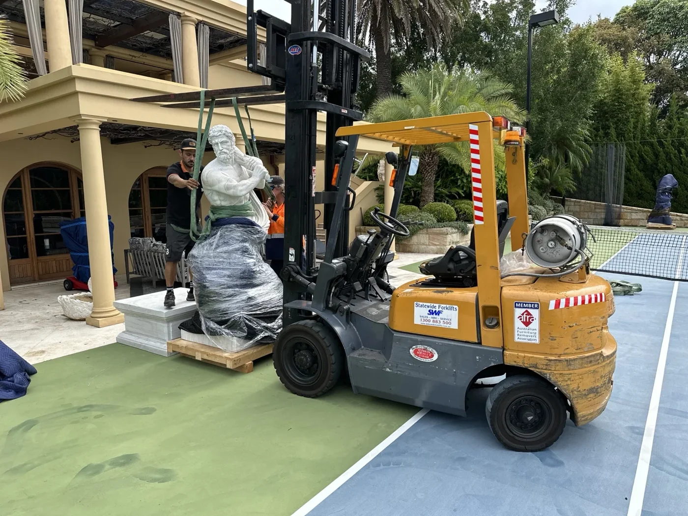 JB crew using a forklift beside an uncovered marble statue and pedestal