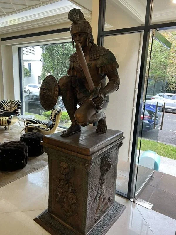 Bronze warrior sculpture and decorative pedestal beside the showroom glass entrance