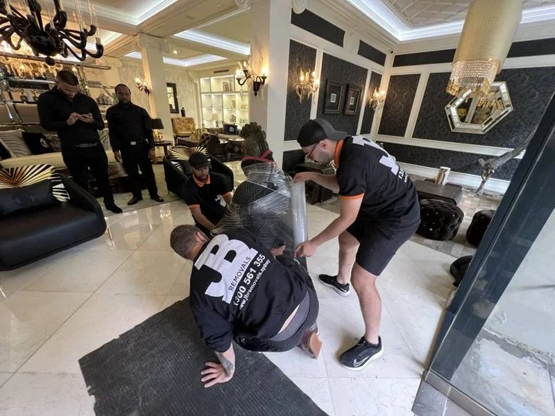 JB removalists adding padding around a blanket-wrapped bronze sculpture beside the showroom doorway