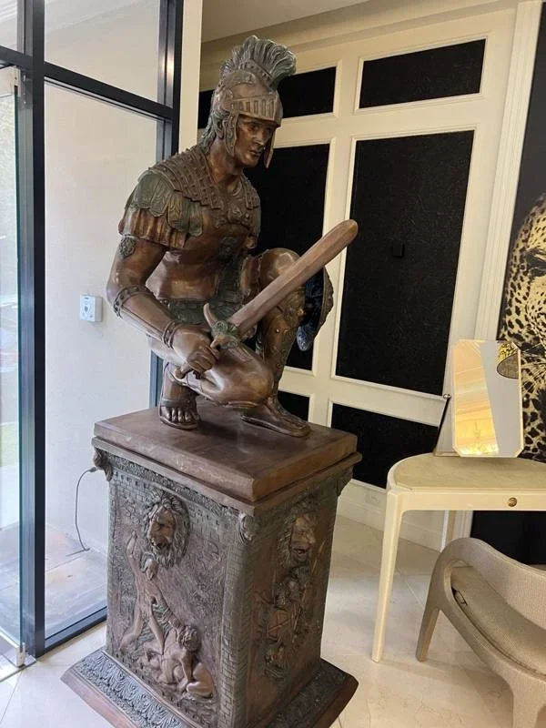 Bronze warrior sculpture with sword and shield on an ornate pedestal inside the showroom