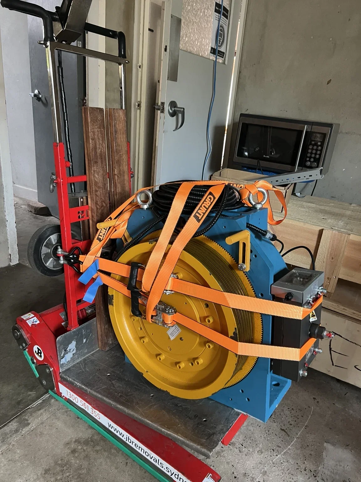 Close view of a lift machinery unit with a yellow grooved wheel, straps and timber backing on a stair climber