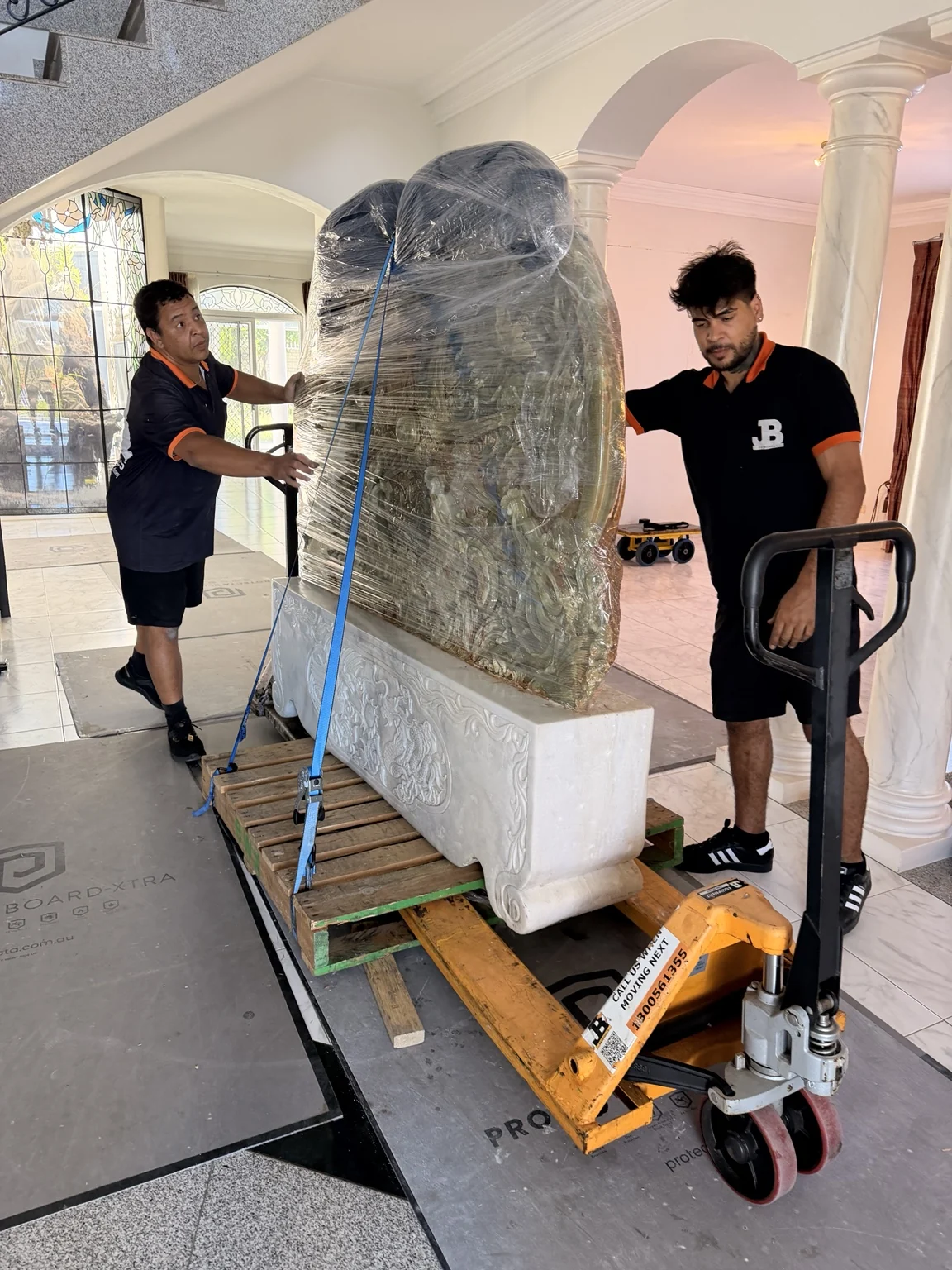 Wrapped stone sculpture secured with blue straps on a supported pallet
