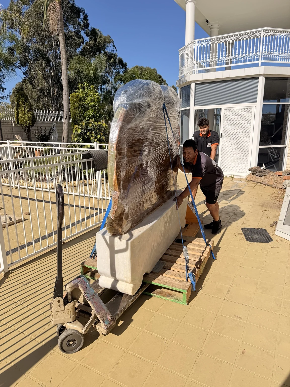 JB removalists guiding a wrapped sculpture through a paved outdoor area