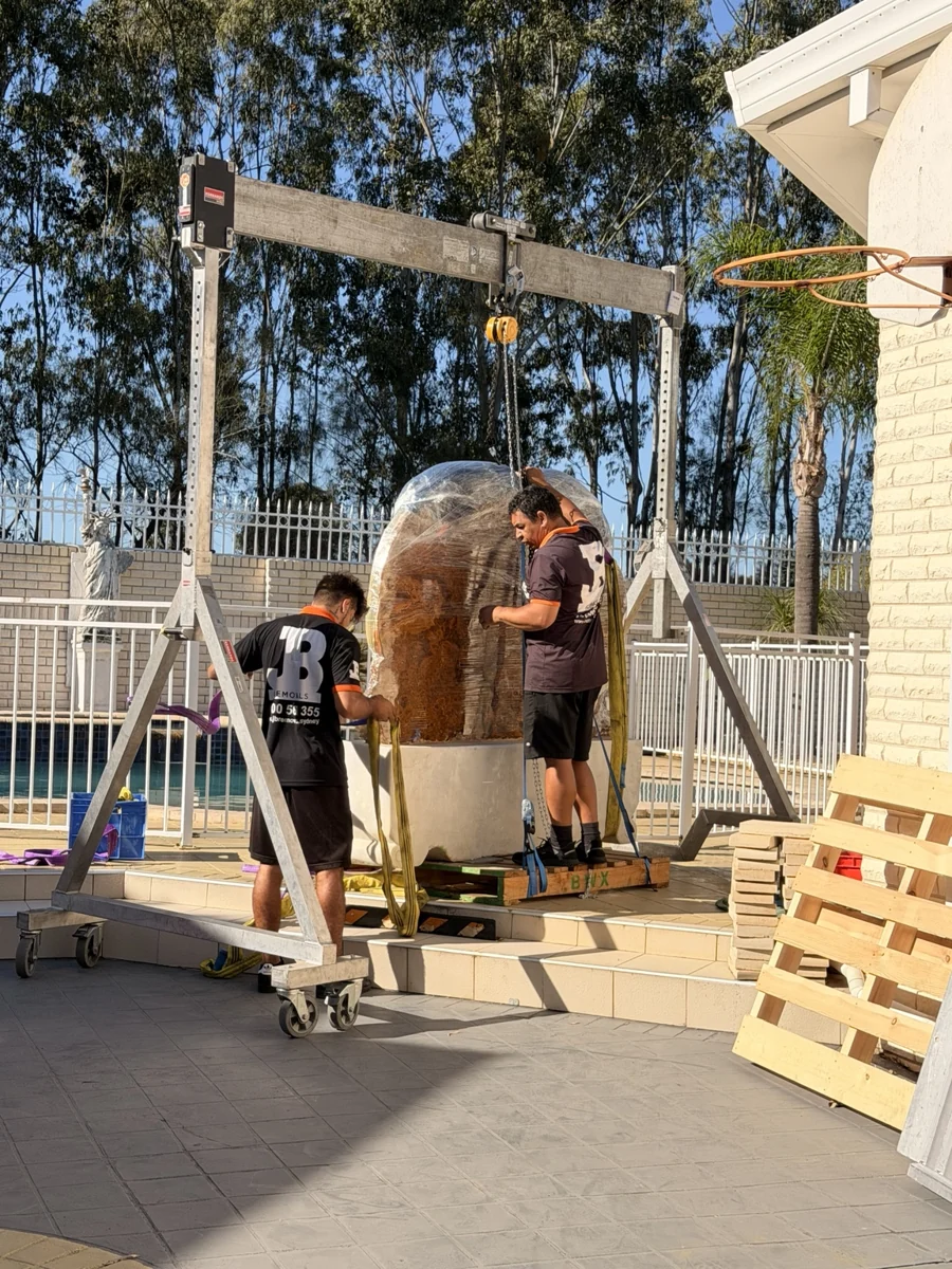 Mobile gantry and chain hoist positioned over a stone sculpture at steps
