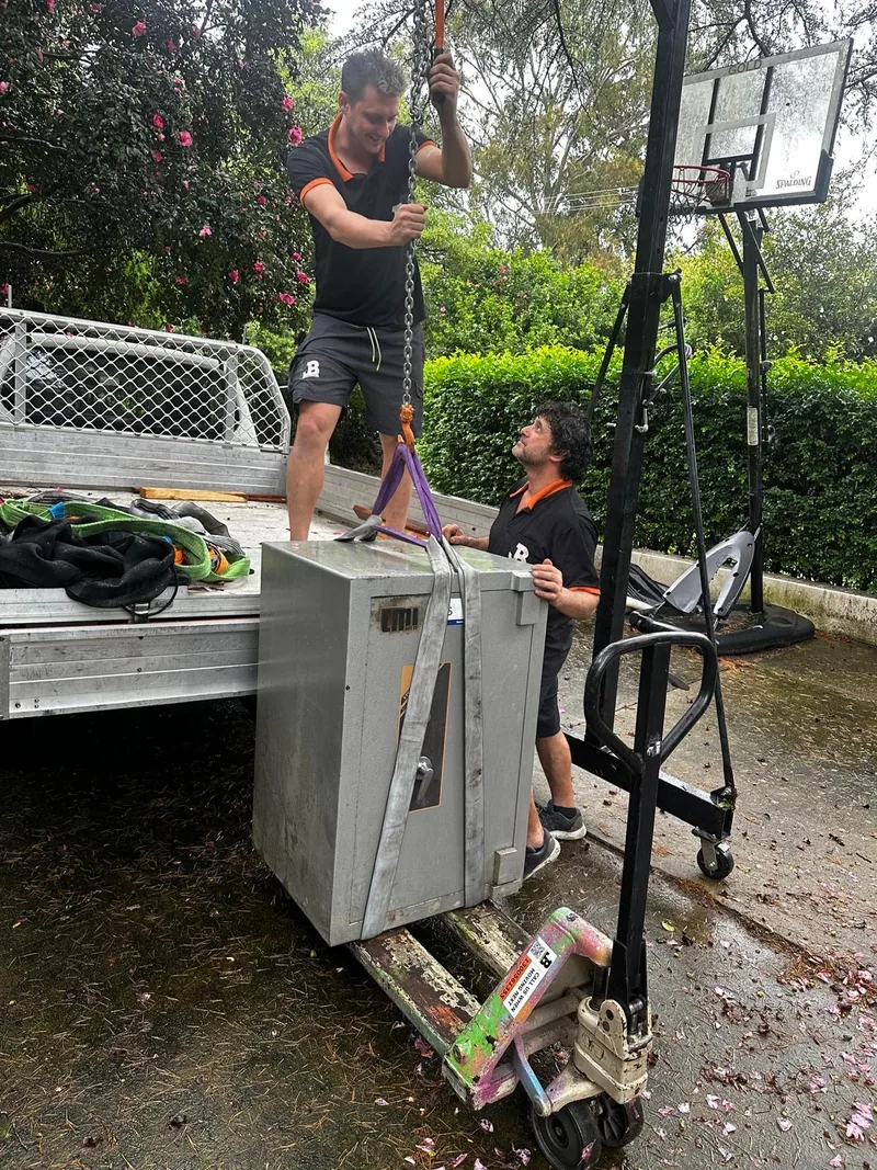 JB Removals crew handling the safe with lifting equipment beside a flatbed truck in Sydney