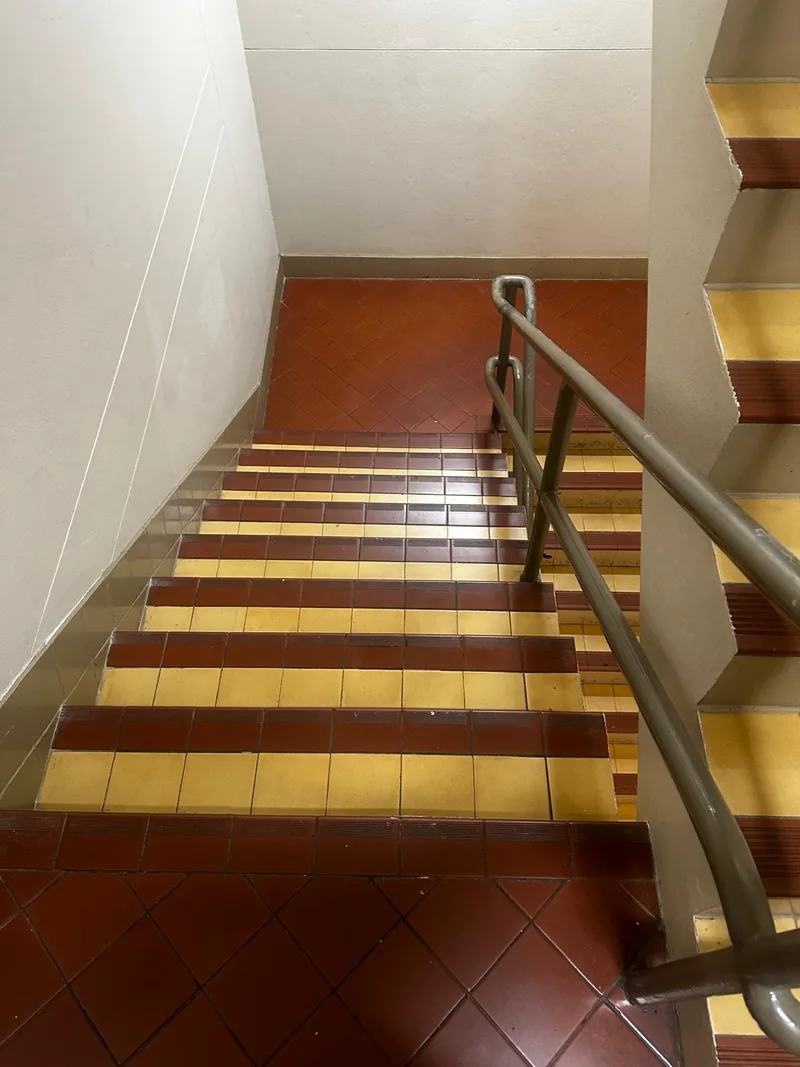 Tiled stair flight with yellow step edges and metal handrails on the safe-moving route