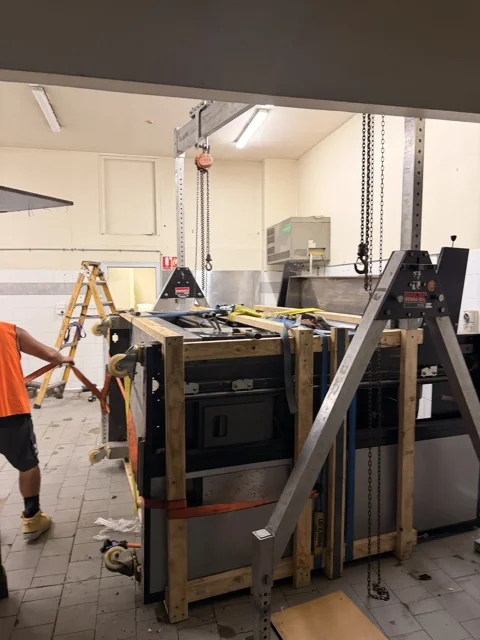 JB Removals: Commercial pizza oven enclosed by timber support framing beneath a gantry with chain hoists