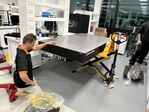 JB Removals: DAEIL SYSTEMS optical table supported on a high-lift scissor pallet jack while the JB team works in a university laboratory