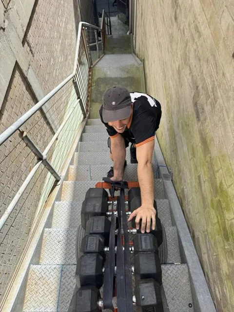JB Removals: JB removalist guiding a strapped load of dumbbells on moving equipment along the metal gym staircase